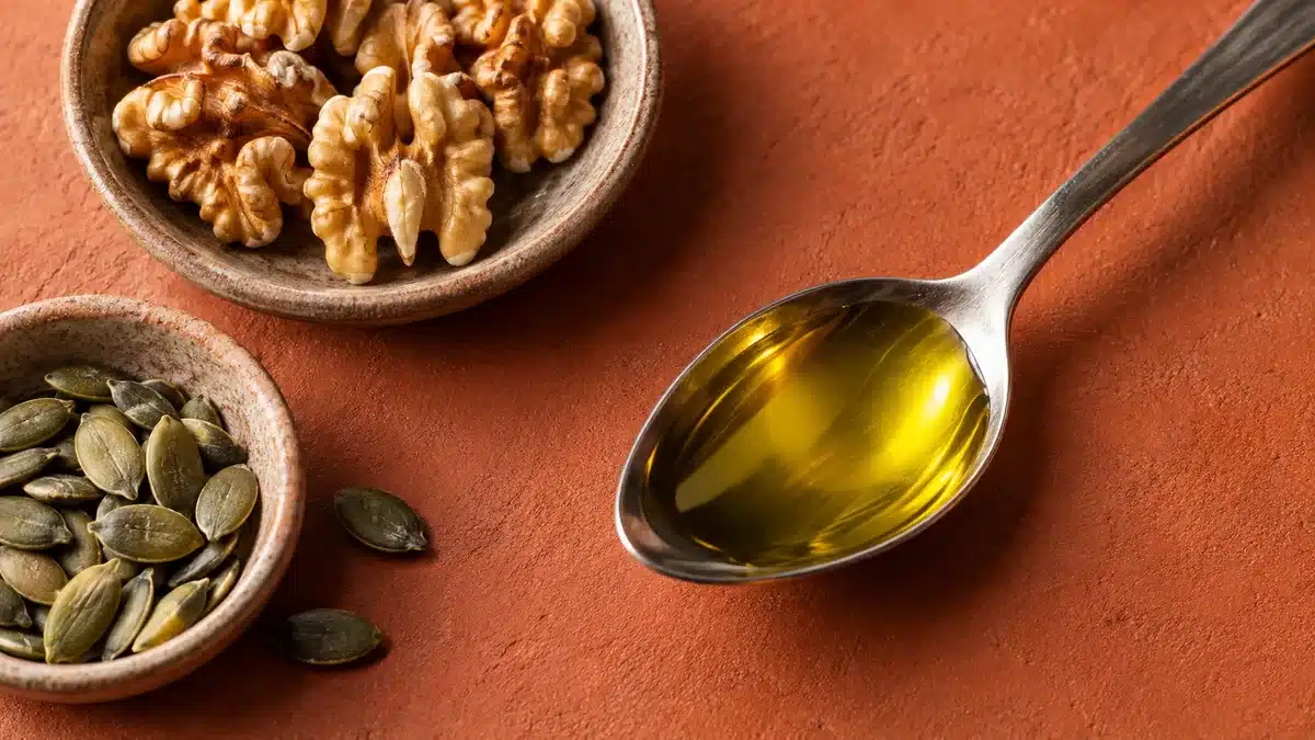 Cuchara con aceite de oliva junto a nueces y semillas de calabaza sobre una superficie terracota